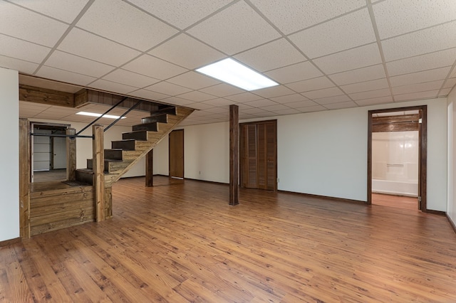 finished below grade area with stairs, baseboards, a drop ceiling, and wood finished floors