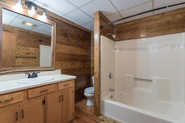 bathroom featuring a paneled ceiling, shower / bathing tub combination, toilet, wooden walls, and vanity