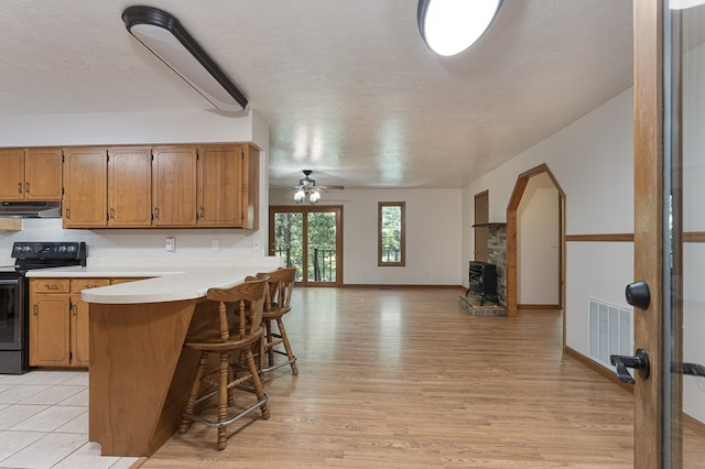 kitchen with visible vents, a breakfast bar, a peninsula, light countertops, and range with electric stovetop