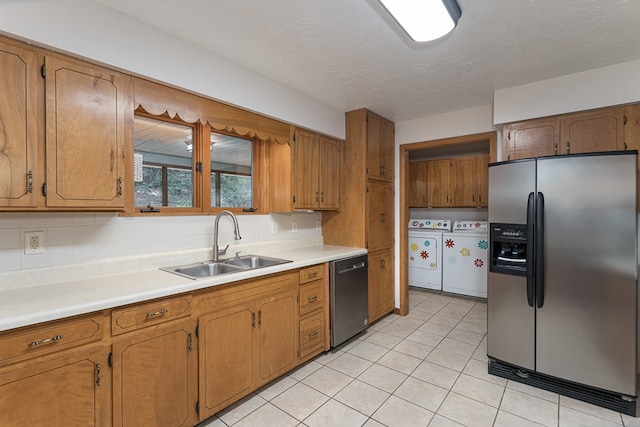 kitchen with a sink, washer and dryer, light countertops, appliances with stainless steel finishes, and brown cabinets