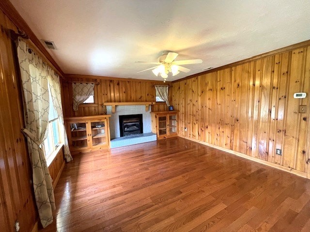 unfurnished living room with crown molding, wood-type flooring, wooden walls, and ceiling fan