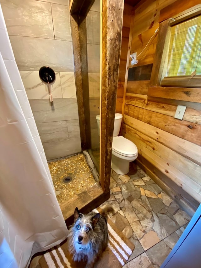 bathroom with curtained shower, wooden walls, and toilet