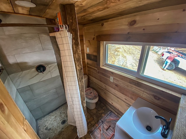 bathroom with toilet, sink, a tile shower, and wood walls