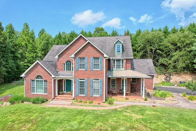 colonial inspired home with brick siding, covered porch, driveway, and a front lawn