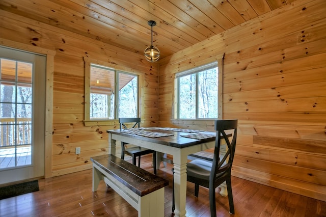 dining space featuring wood-type flooring, wooden walls, a healthy amount of sunlight, and wooden ceiling