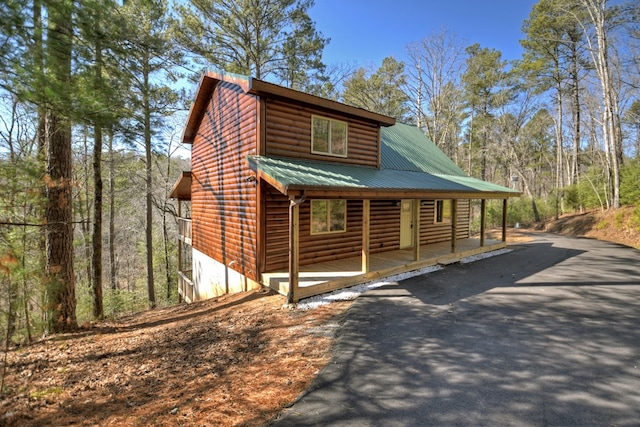 view of front of home featuring covered porch, driveway, metal roof, and log veneer siding