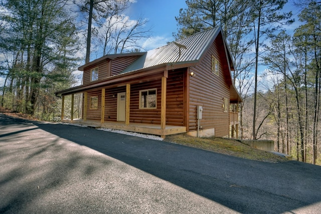 view of side of home featuring faux log siding, covered porch, driveway, and metal roof