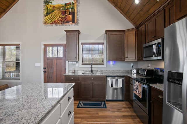 kitchen with dark wood finished floors, wooden ceiling, appliances with stainless steel finishes, light stone countertops, and a sink