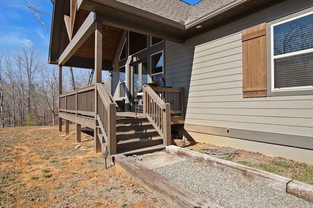 doorway to property featuring a wooden deck and roof with shingles