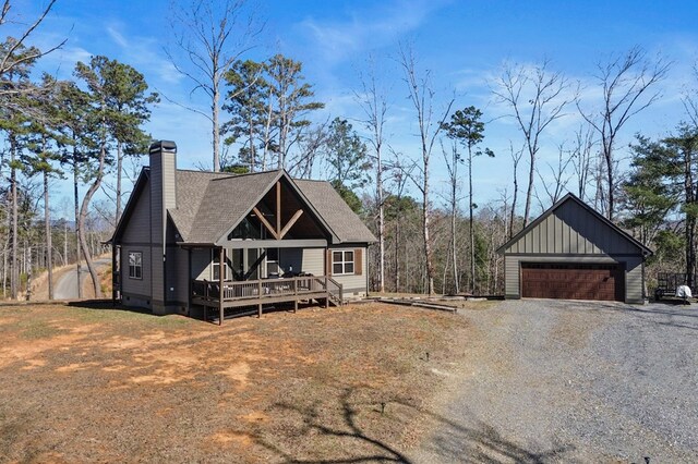 view of front of home with roof with shingles, a detached garage, a chimney, board and batten siding, and a wooden deck