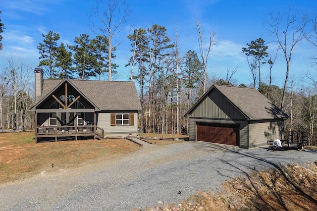 view of front of house featuring a deck, an outbuilding, a garage, a shingled roof, and a chimney