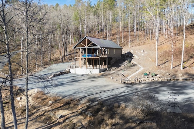 chalet / cabin with aphalt driveway, metal roof, a deck, and a forest view