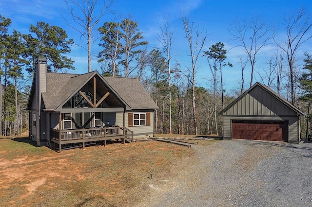 view of front of property featuring a detached garage, a chimney, a shingled roof, board and batten siding, and a front lawn