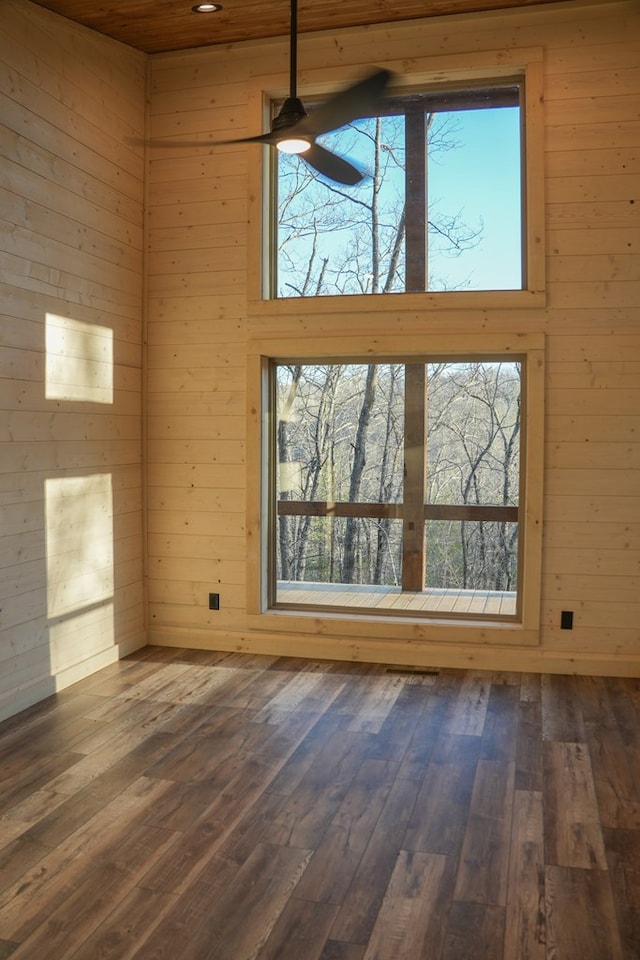 unfurnished living room featuring a towering ceiling, wood-type flooring, ceiling fan, and wood walls