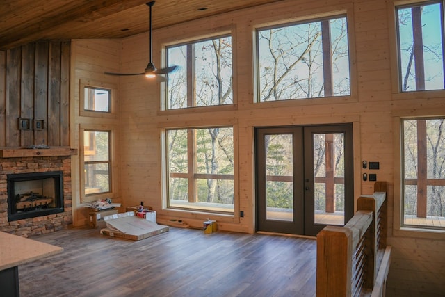 unfurnished living room with dark wood-type flooring, a stone fireplace, french doors, and a high ceiling