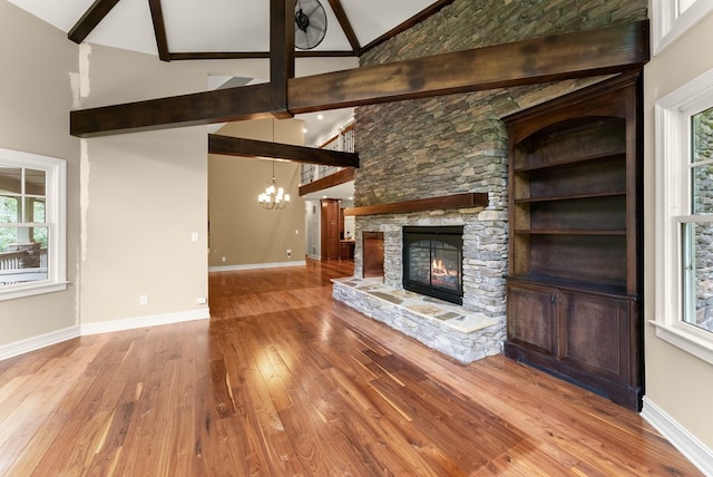 802 Old Mill Trl, Ball Ground, GA 30107 - unfurnished living room featuring a chandelier, a stone fireplace, high vaulted ceiling, wood-type flooring, and beamed ceiling
