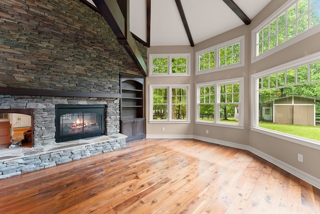 802 Old Mill Trl, Ball Ground, GA 30107 - unfurnished living room featuring beamed ceiling, baseboards, high vaulted ceiling, wood finished floors, and a stone fireplace