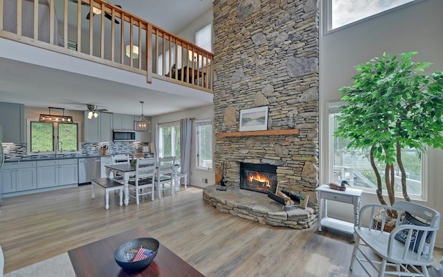 living room with ceiling fan, sink, light hardwood / wood-style flooring, a fireplace, and a towering ceiling