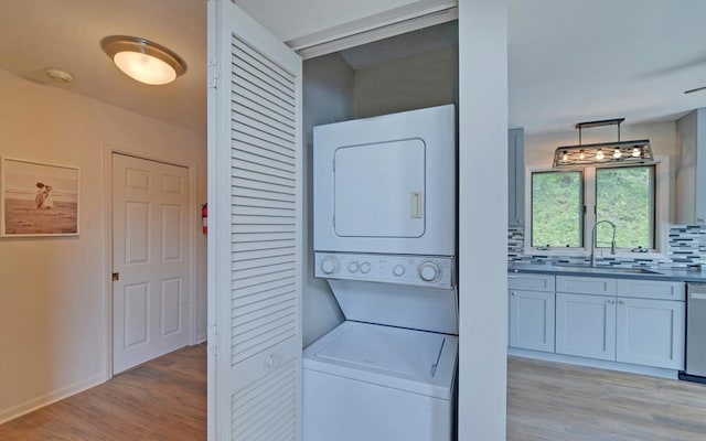 laundry room with sink, light hardwood / wood-style flooring, and stacked washer / drying machine