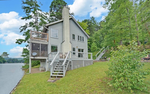 back of house with a sunroom, a yard, and a deck with water view