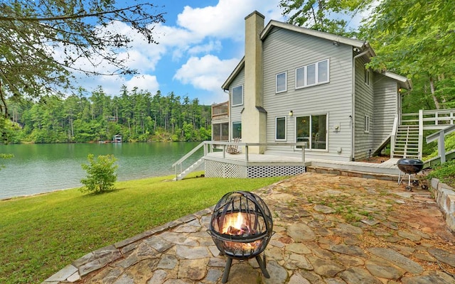 back of property featuring a patio area, a lawn, a deck with water view, and an outdoor fire pit