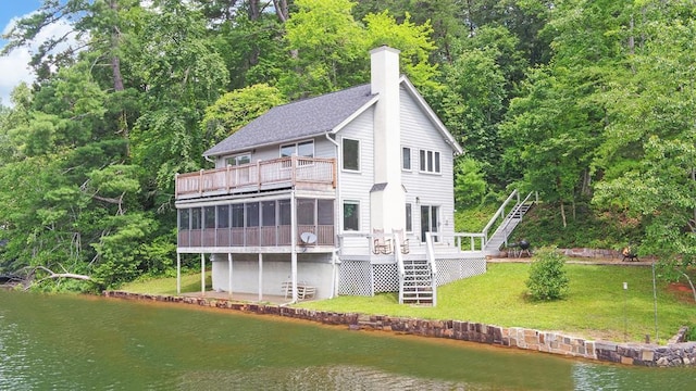 rear view of house with a yard, a sunroom, and a deck with water view