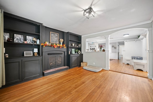 unfurnished living room featuring light hardwood / wood-style floors, crown molding, decorative columns, and built in shelves