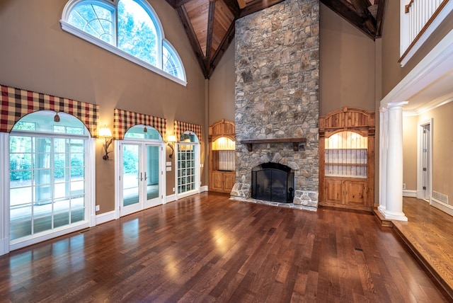 unfurnished living room with french doors, a stone fireplace, decorative columns, a towering ceiling, and wood-type flooring