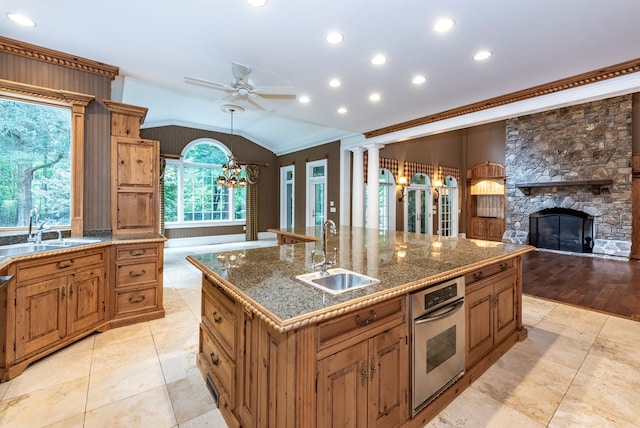 kitchen featuring sink, an island with sink, oven, vaulted ceiling, and a fireplace