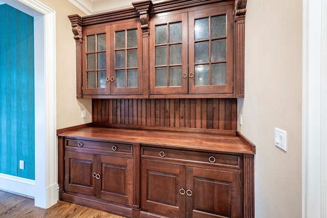 bar with dark brown cabinets, light hardwood / wood-style floors, and crown molding