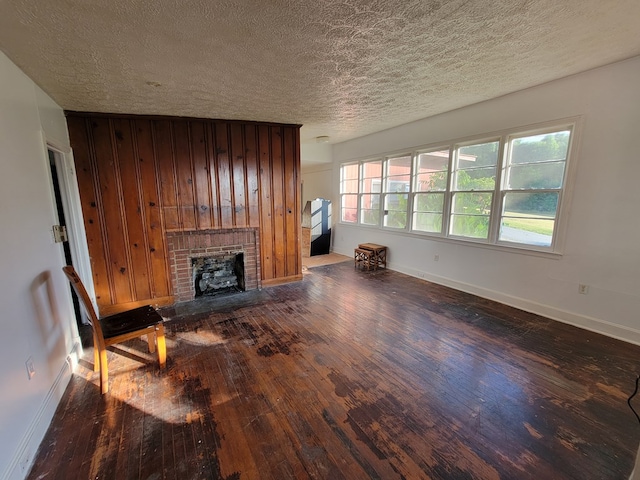 unfurnished living room with a textured ceiling, dark hardwood / wood-style flooring, a brick fireplace, and wooden walls