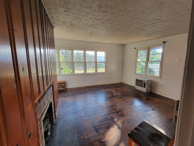 unfurnished living room with heating unit, a wealth of natural light, dark hardwood / wood-style floors, and a textured ceiling