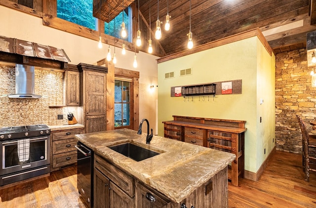 kitchen with backsplash, stainless steel gas range oven, a sink, dark wood-style floors, and wall chimney exhaust hood
