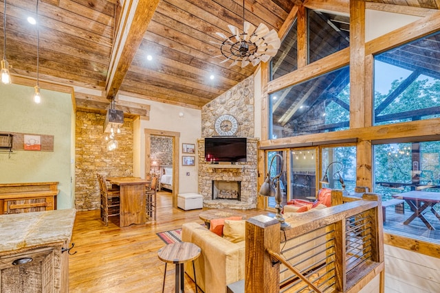 living area with beam ceiling, a fireplace, high vaulted ceiling, light wood-style flooring, and wood ceiling
