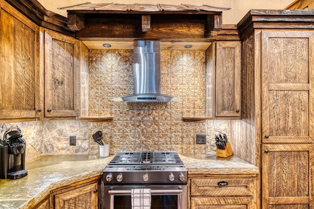 kitchen with brown cabinetry, gas range, light countertops, wall chimney exhaust hood, and backsplash