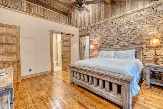 bedroom featuring connected bathroom, high vaulted ceiling, a barn door, and hardwood / wood-style flooring