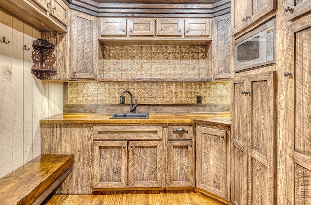 kitchen with a sink, light wood finished floors, wooden counters, stainless steel microwave, and decorative backsplash