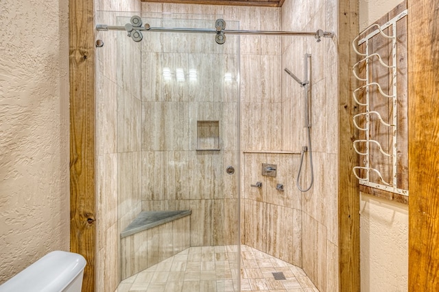 bathroom with a textured wall, a tile shower, and toilet