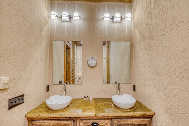 full bathroom with a sink, a textured wall, and double vanity