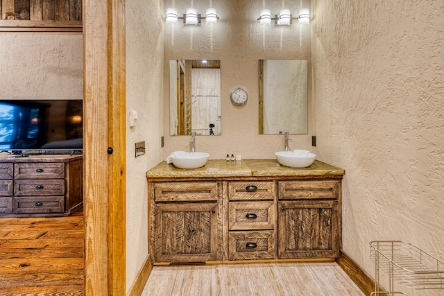 bathroom with a textured wall, a sink, and wood finished floors