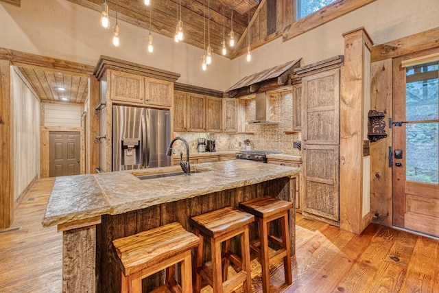 kitchen featuring decorative backsplash, a towering ceiling, a sink, stainless steel appliances, and wall chimney exhaust hood