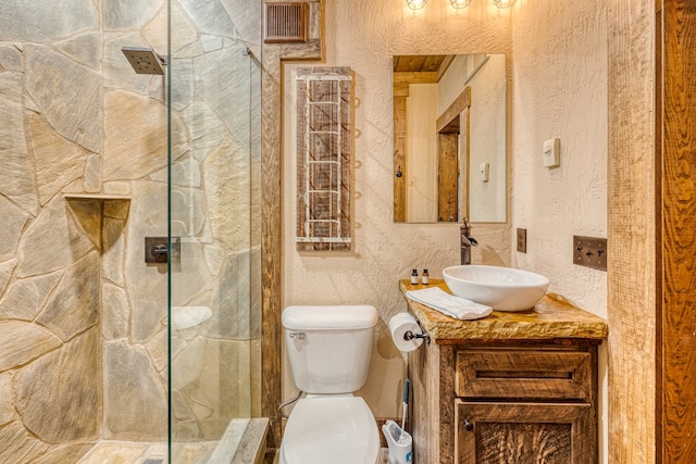 full bath with vanity, a shower with door, a textured wall, and toilet