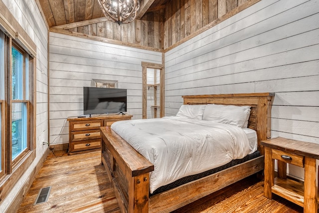 bedroom with wooden walls, a chandelier, hardwood / wood-style floors, lofted ceiling, and visible vents