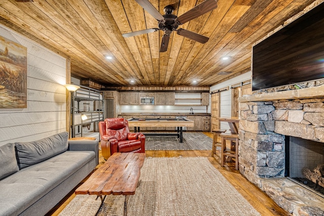living room featuring wood ceiling, a stone fireplace, wood walls, light wood-type flooring, and a barn door