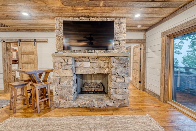 unfurnished living room with a ceiling fan, wood walls, a barn door, wood finished floors, and wooden ceiling
