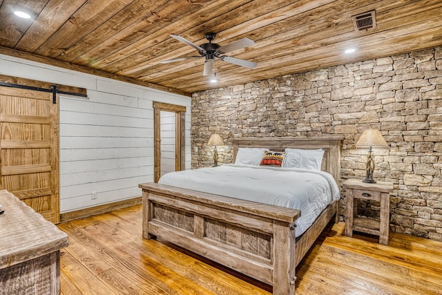 bedroom with a barn door, light wood-style flooring, a ceiling fan, visible vents, and wood ceiling