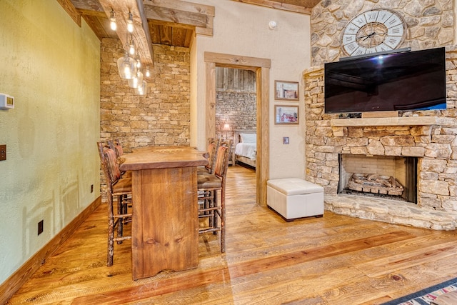bar with baseboards, a textured wall, a stone fireplace, and wood finished floors