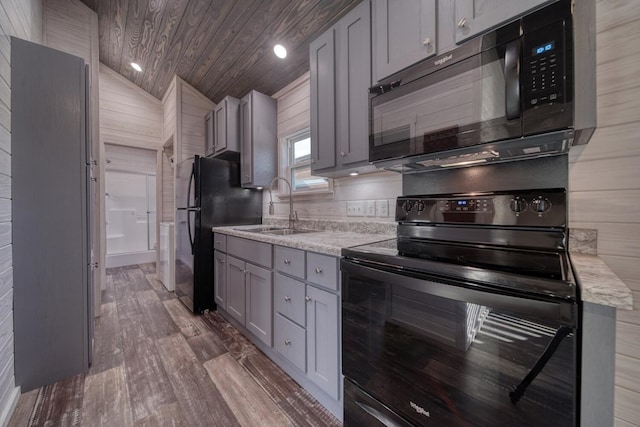 kitchen featuring lofted ceiling, sink, black appliances, gray cabinets, and hardwood / wood-style flooring