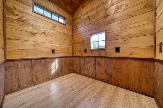 spare room featuring lofted ceiling, wooden walls, and light hardwood / wood-style flooring