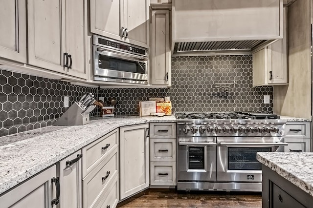 kitchen featuring tasteful backsplash, light stone counters, range with two ovens, and premium range hood